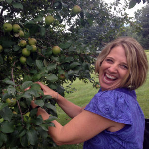 A photo of Kaye House-Agar, or "Coach K," all smiles and picking citrus fruit from a tree